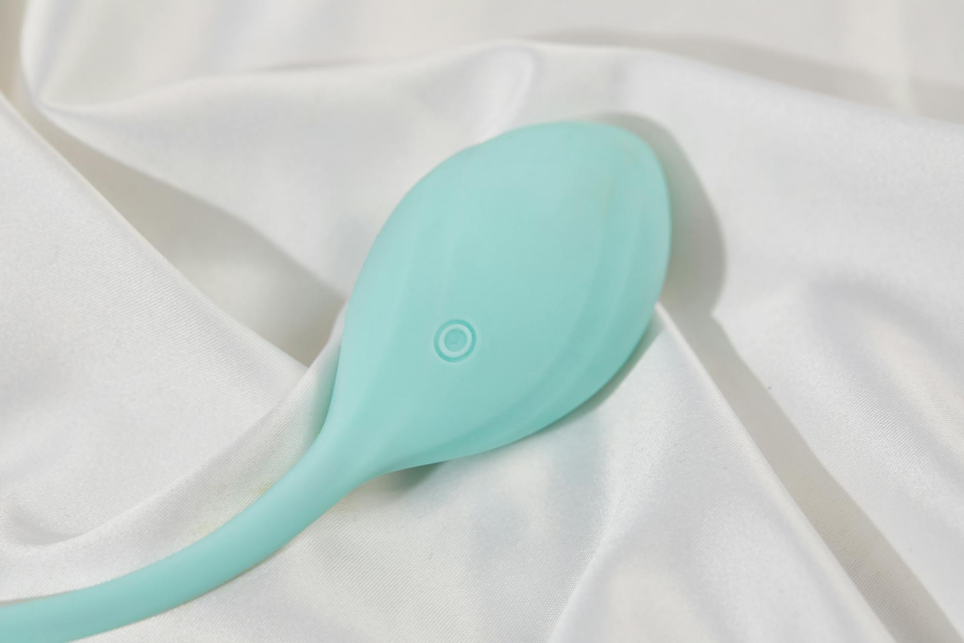 A stylish teal clitoral vibrator resting on soft white silk, symbolizing intimate exploration