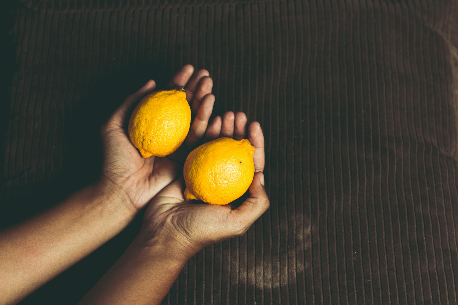 A hand holding a fresh lemon on a soft pink background, symbolizing delicate sensation and exploration.