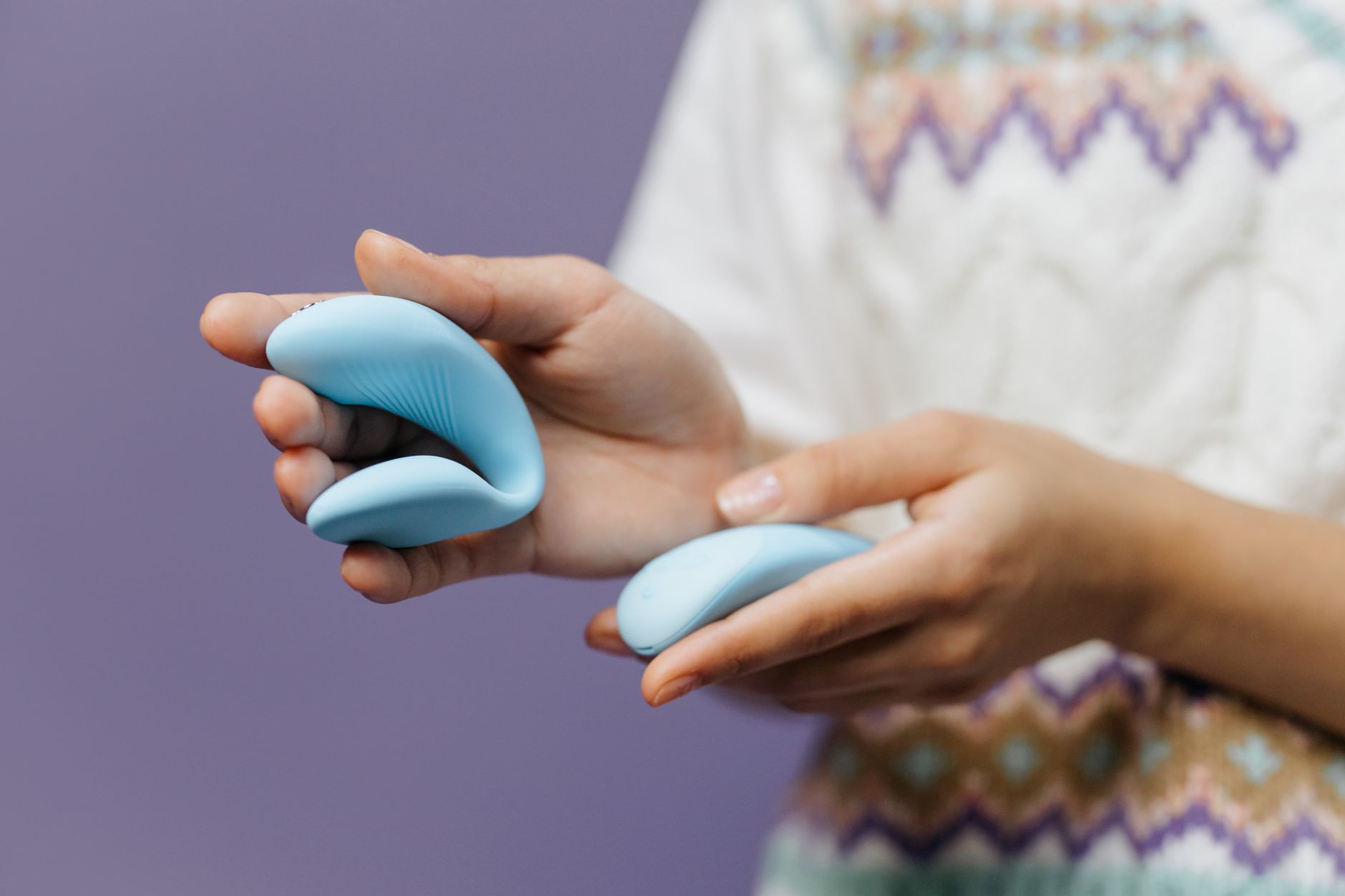 Close-up of hands holding a lemon vibrator against a purple background