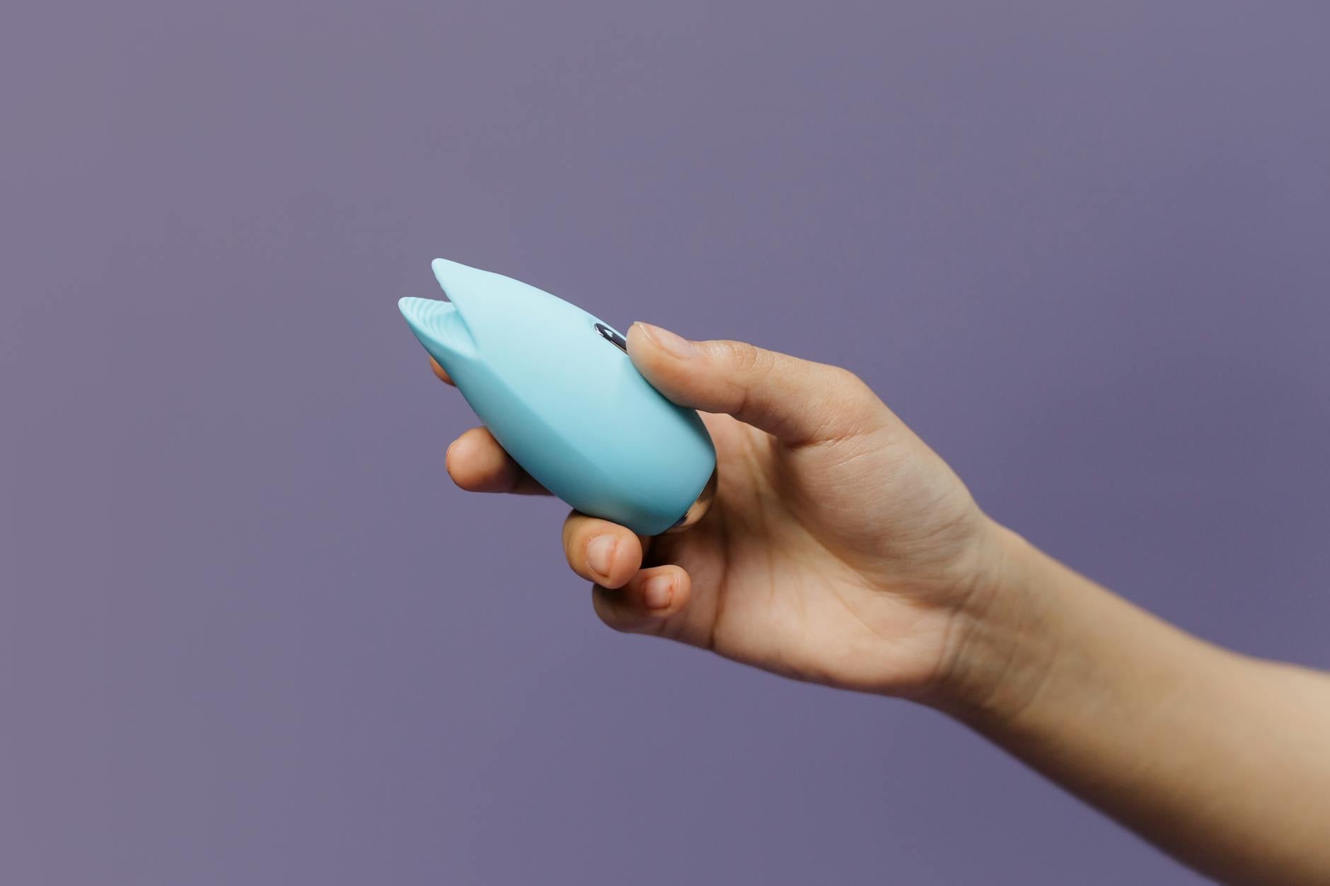 Woman holding blue and pink silicone vibrators in a moment of contemplation and choice