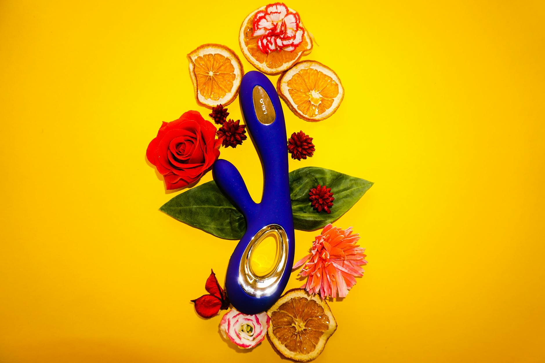 Blue lemon vibrator surrounded by flowers and fresh citrus on a bright yellow background