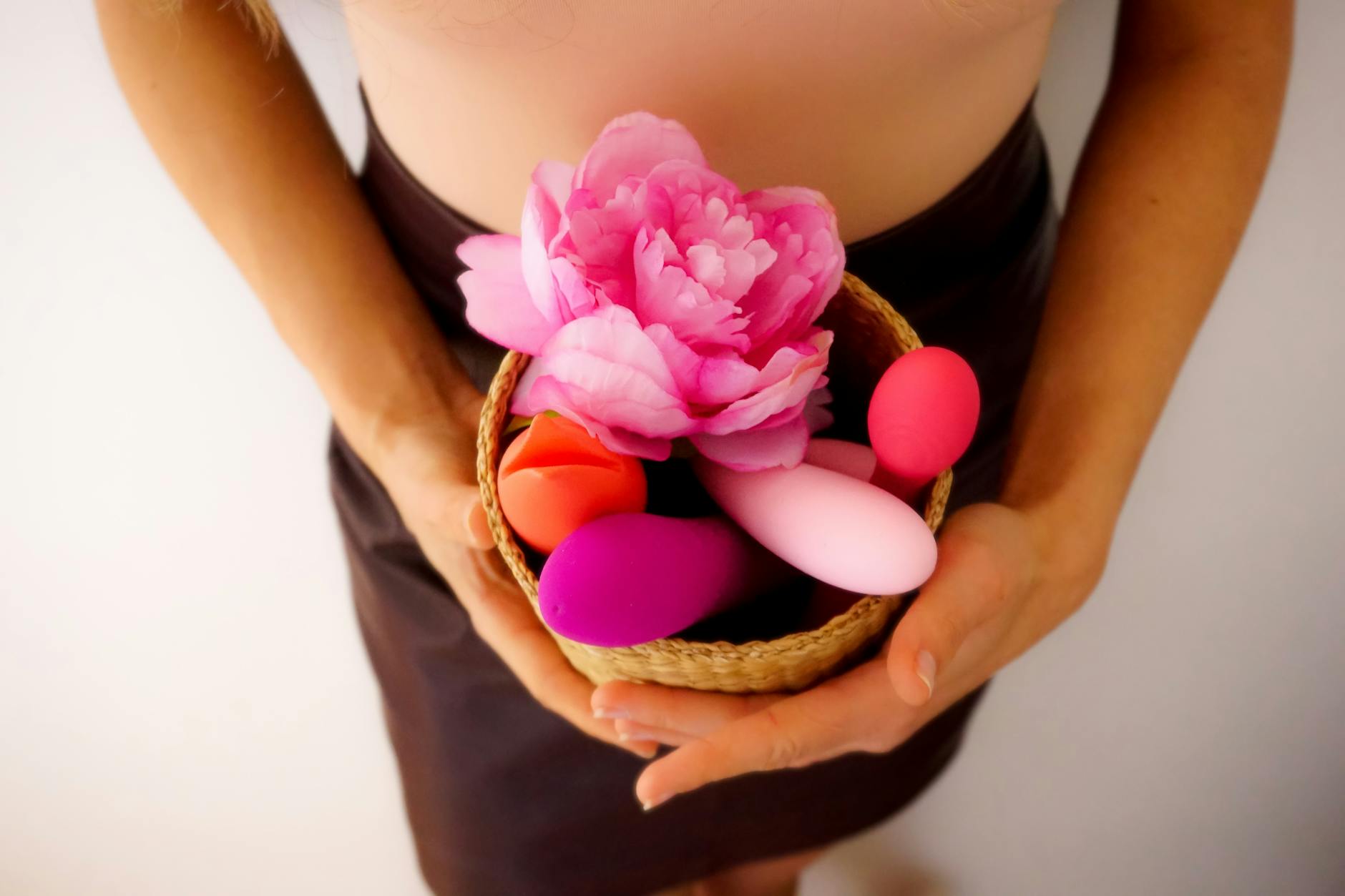 Two hands holding pink and blue silicone vibrators against a pastel background.